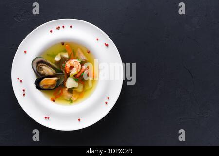 Soupe de fruits de mer avec des crevettes, des moules et des légumes dans un bol blanc sur un fond sombre Banque D'Images