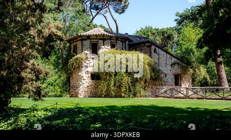 Un charmant chalet rustique niché dans la verdure luxuriante du parc El Capricho, Madrid, Espagne. Cette structure en pierre est entourée d'arbres vibrants. Banque D'Images