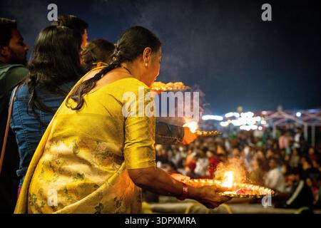 Femme indienne dans le saree jaune exécute aarti avec des lampes à huile lors d'une cérémonie de festival nocturne animée. Banque D'Images