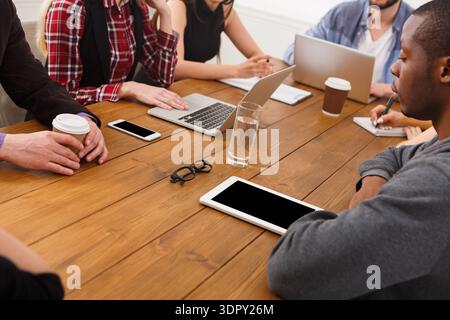 Groupe de personnes en réunion discutant des tâches à une table en bois avec des appareils et des boissons Banque D'Images