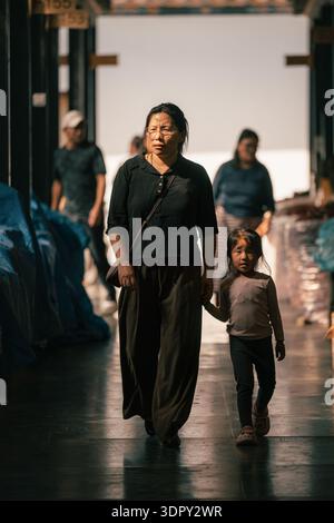 Thimphu, Bhoutan - 27 septembre 2025 : vue d'une mère et d'un enfant marchant main dans la main à travers le marché agricole du centenaire, la lumière projetant de longues ombres Banque D'Images