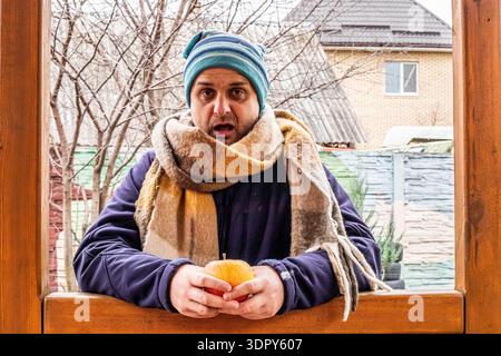 Un homme surpris dans un chapeau rayé tient une pomme dorée mûre dehors. Banque D'Images