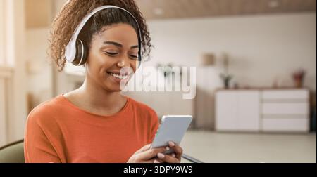 Jeune femme aime la musique et les chats sur smartphone tout en portant des écouteurs dans une pièce lumineuse Banque D'Images