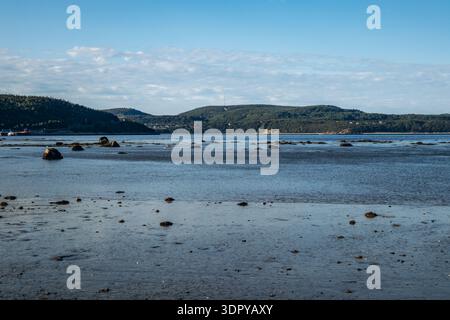 Paysages à marée basse le long des plages de la Baie Sainte Catherine avec rivage sablonneux et galets, eau peu profonde calme, rochers éparpillés et colline boisée Banque D'Images