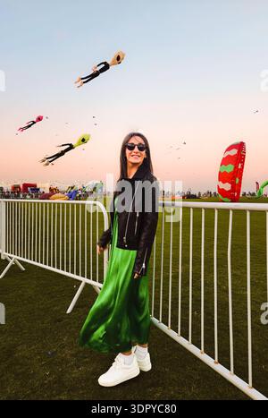 Doha, Qatar - 22 janvier 2026 : femme pose avec des cerfs-volants géants colorés volant au-dessus d'un parc public pendant le festival de cerf-volant de Doha au coucher du soleil. Populaire célèbre Cul Banque D'Images