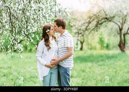 Portrait de beaux futurs parents embrassant pendant le coucher du soleil sur fond de pommier de la nature Banque D'Images