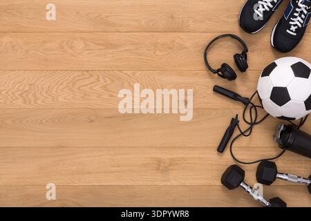 Équipement sportif disposé sur un plancher en bois avec écouteurs, haltères et ballon de football Banque D'Images