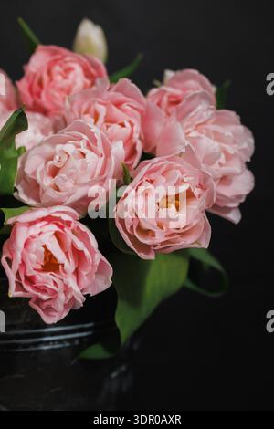 Une nature morte sophistiquée avec un bouquet de tulipes roses de style pivoine (Tulipa gesneriana) disposées dans un seau en métal foncé Banque D'Images