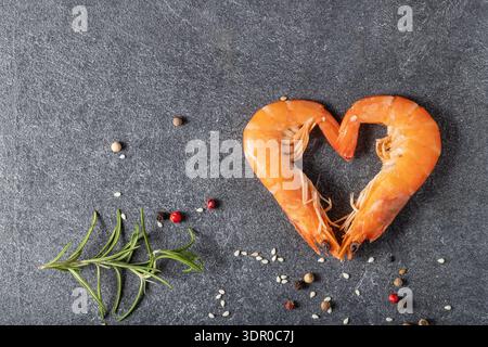 Coeur de deux crevettes tigrées bouillies avec poivre et herbe de romarin sur planche de pierre sombre. Carte vue de dessus avec espace de copie Banque D'Images