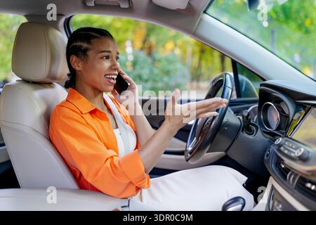 Jeune femme noire parlant au téléphone portable tout en conduisant une voiture, faisant des gestes émotionnels Banque D'Images