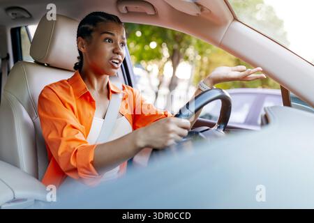 Jeune femme noire conduisant une voiture avec une expression surprise et questionnant Banque D'Images