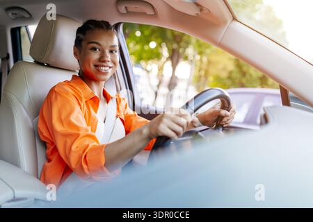 Jeune femme noire conduisant la voiture et souriant à la caméra avec une posture confiante Banque D'Images