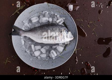 Poisson frais placé sur de la glace avec assaisonnement sur une assiette avant cuisson Banque D'Images