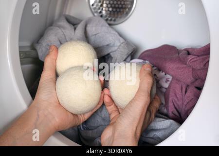 Gros plan main de femme plaçant des boules de séchage de laine réutilisables dans le sèche-linge domestique. Concept de routine de blanchisserie écologique favorisant un mode de vie durable, Banque D'Images