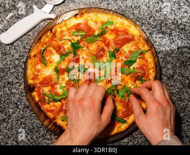 Mains préparer une Pizza fraîchement préparée avec des garnitures dans un cadre de cuisine Banque D'Images