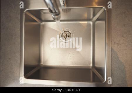 L'eau coule du robinet dans l'évier en acier inoxydable Banque D'Images