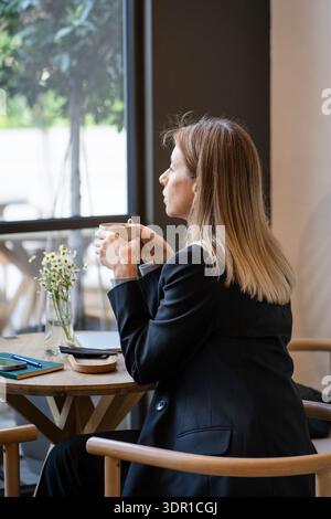 Femme d'affaires réfléchie appréciant boire du café au restaurant après une journée productive au travail. Banque D'Images