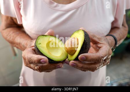 Moitiés d'avocat fraîches et mûres avec PIT : un super-aliment sain. Gros plan des mains tenant un avocat mûr, montrant sa texture crémeuse et sa fosse. Idéal pour nutr Banque D'Images