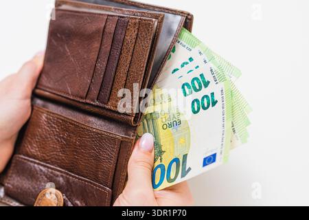 Femme mettant 100 billets de banque en euros dans un sac à main brun à la maison. Planification financière, revenu salarial, épargne, gestion de l'argent et concept de budget du ménage. Banque D'Images