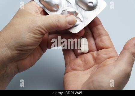 Mains de la personne poussant une pilule ovale blanche hors d'un emballage blister en argent dans la paume ouverte, en se concentrant sur la santé et le traitement Banque D'Images