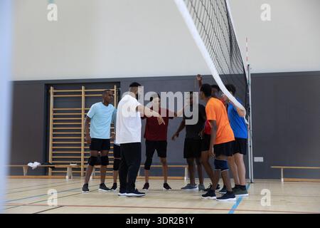 Équipe masculine diversifiée de volleyball rassemblant, écoutant, faisant des gestes et portant des vêtements de sport par filet dans la salle de gym Banque D'Images