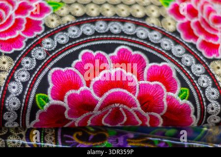 Gros plan de broderie florale colorée avec des fleurs roses ressemblant à des pivoines, des feuilles vertes et des bandes décoratives concentriques sur un tissu sombre, montrant des s détaillés Banque D'Images