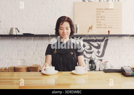 Le barista sert deux tasses de café dans un café au design minimaliste et au comptoir en bois Banque D'Images