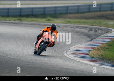 Vue de trois quarts avant d'un pilote de moto en cuirs orange et noir penchant une moto sport orange dans un virage sur une course professionnelle c Banque D'Images