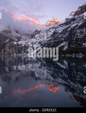 Vue des sommets de montagne enneigés enflammés par la douce lueur de l'aube, reflétée dans les eaux calmes, créant une symphonie de lumière et d'ombre, Airolo, T. Banque D'Images