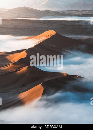 Vue aérienne des dunes dorées s'élèvent majestueusement au-dessus d'une mer de brouillard éthérée, créant des contrastes frappants entre la lumière et l'ombre, Sossusvlei, Hardap Regio Banque D'Images