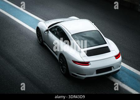 Vue arrière à angle élevé d'une voiture de sport blanche performante conduisant sur une piste de course avec des marques bleues et blanches. Banque D'Images