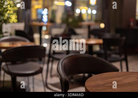 intérieur de café confortable floue la nuit avec des lumières bokeh chaudes, des tables en bois et d'élégantes chaises sombres, fond parfait pour les thèmes de restaurant ou de bistrot Banque D'Images