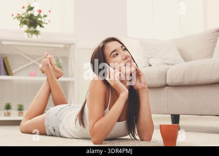 Femme se trouve sur le sol tout en parlant sur le téléphone dans le cadre confortable de salon Banque D'Images
