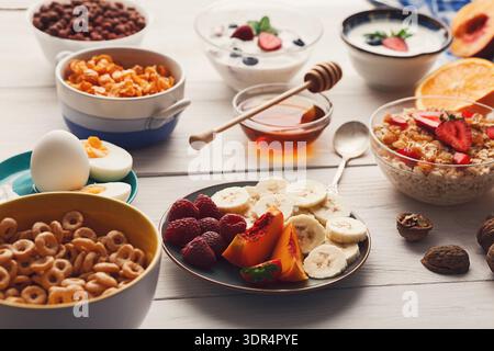 Petit déjeuner lumineux avec fruits, céréales, yaourt et noix sur une table en bois Banque D'Images