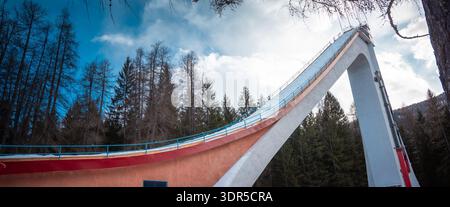 Rampe de saut à ski s'élevant au-dessus de la forêt alpine à Cortina d Ampezzo, en Italie, avec une structure en béton spectaculaire, un ciel bleu, la lumière de l'hiver et des pins imposants Banque D'Images