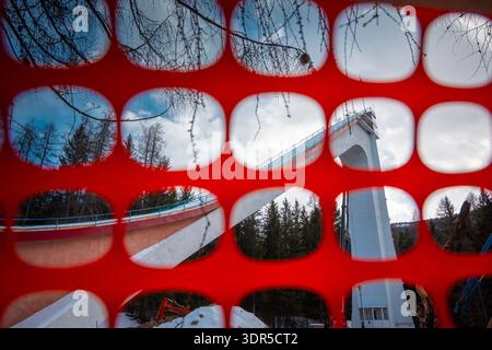 Tour de saut à ski à Cortina d Ampezzo vue à travers le filet de sécurité rouge, créant un cadre géométrique audacieux avec des arbres alpins, structure en béton, hiver Banque D'Images