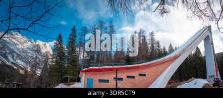 Rampe de saut à ski s'élevant au-dessus de la forêt alpine à Cortina d Ampezzo, en Italie, avec une structure en béton spectaculaire, un ciel bleu, la lumière de l'hiver et des pins imposants Banque D'Images