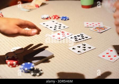 Mains, cartes et jetons de poker sur une table lors d'un jeu de poker à domicile occasionnel, capturant le jeu social, la stratégie et le divertissement à l'intérieur Banque D'Images