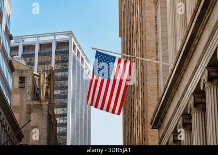 Les États-Unis signalent des vagues entre les grands bâtiments de la ville par une journée ensoleillée, montrant l'identité nationale, l'architecture urbaine et l'atmosphère patriotique dans Downto Banque D'Images