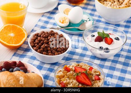 Le petit-déjeuner se compose de fruits, de céréales et de yaourt sur une nappe à carreaux bleue Banque D'Images