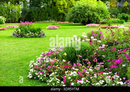 Jardin paysager avec des parterres de fleurs vibrantes, des plantes en fleurs et une pelouse verdoyante dans un parc ensoleillé. Décor estival lumineux avec arbustes ornementaux Banque D'Images
