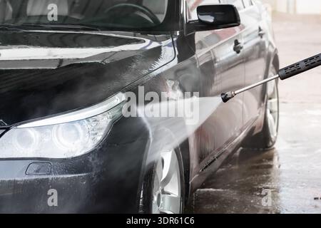 Un homme lave sa voiture dans un lave-auto en libre-service. La voiture est lavée avec de l'eau à haute pression. Lave-auto en libre-service. Banque D'Images