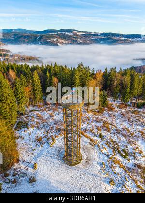 La tour de guet Svetly vrch se dresse à Albrechtice, entourée de neige et d'arbres. La tour offre une vue sur les montagnes et le brouillard en contrebas. Les visiteurs explorent la région au milieu de la nature en hiver. Banque D'Images