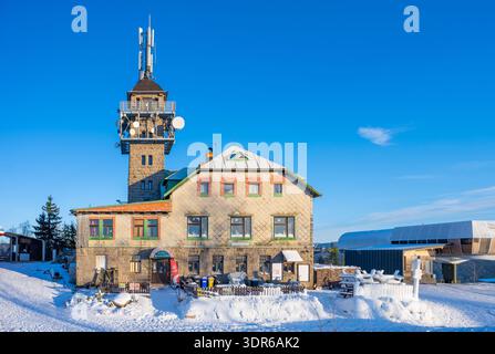 La tour Tanvaldsky Spicak Lookout est haute en hiver. La neige recouvre le sol et les bâtiments. Les visiteurs apprécient la zone de station de montagne à Jizera. Ciel dégagé saluent la journée. Banque D'Images