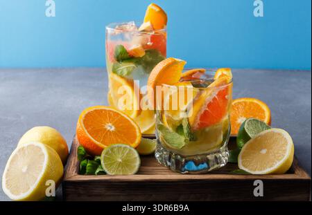 Boissons rafraîchissantes aux fruits avec citron, orange et menthe sur un plateau en bois par un fond bleu Banque D'Images