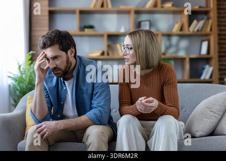 Couple dans un silence tendu sur un canapé de salon après une dispute, l'homme tenant sa tête pendant que la femme parle, représentant le stress, la rupture de communication an Banque D'Images