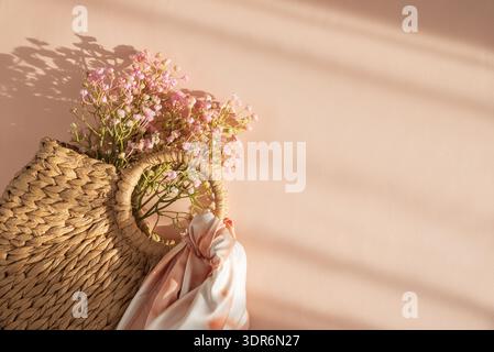 Sac à main en paille tissée avec écharpe soyeuse et fleurs. Élégant été Fashion Flatlay sur fond de pêche Banque D'Images