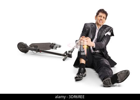 Homme d'affaires blessé dans un costume déchiré assis à côté d'un scooter électrique tombé isolé sur fond blanc Banque D'Images