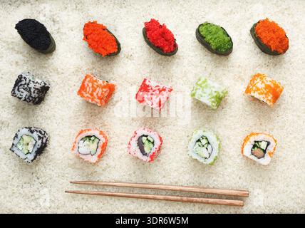 Rouleaux de Sushi colorés et garnitures soigneusement disposés sur une surface blanche pour un repas Banque D'Images