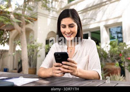 Heureuse jeune femme d'affaires hispanique utilisant le téléphone portable Banque D'Images